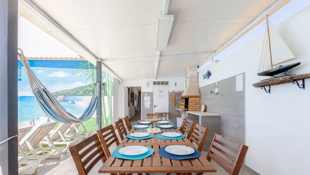 A dining area with a view of the sea, a hammock, and a kitchen in the background. - Bambus House Holidays Rental (Loulé)
