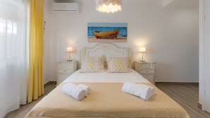 A neatly arranged bedroom with a bed, two bedside tables, a painting of a boat on water, and a hanging light fixture. - Bambus House Holidays Rental (Loulé)