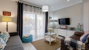 A modern living room with a sofa, a coffee table, a TV, and a dining area. - Bambus House Holidays Rental (Loulé)