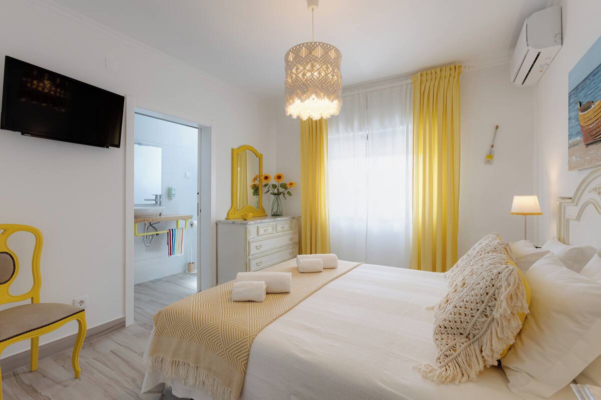 A hotel room with a bed, a television, a mirror, a dresser, and a window with curtains.