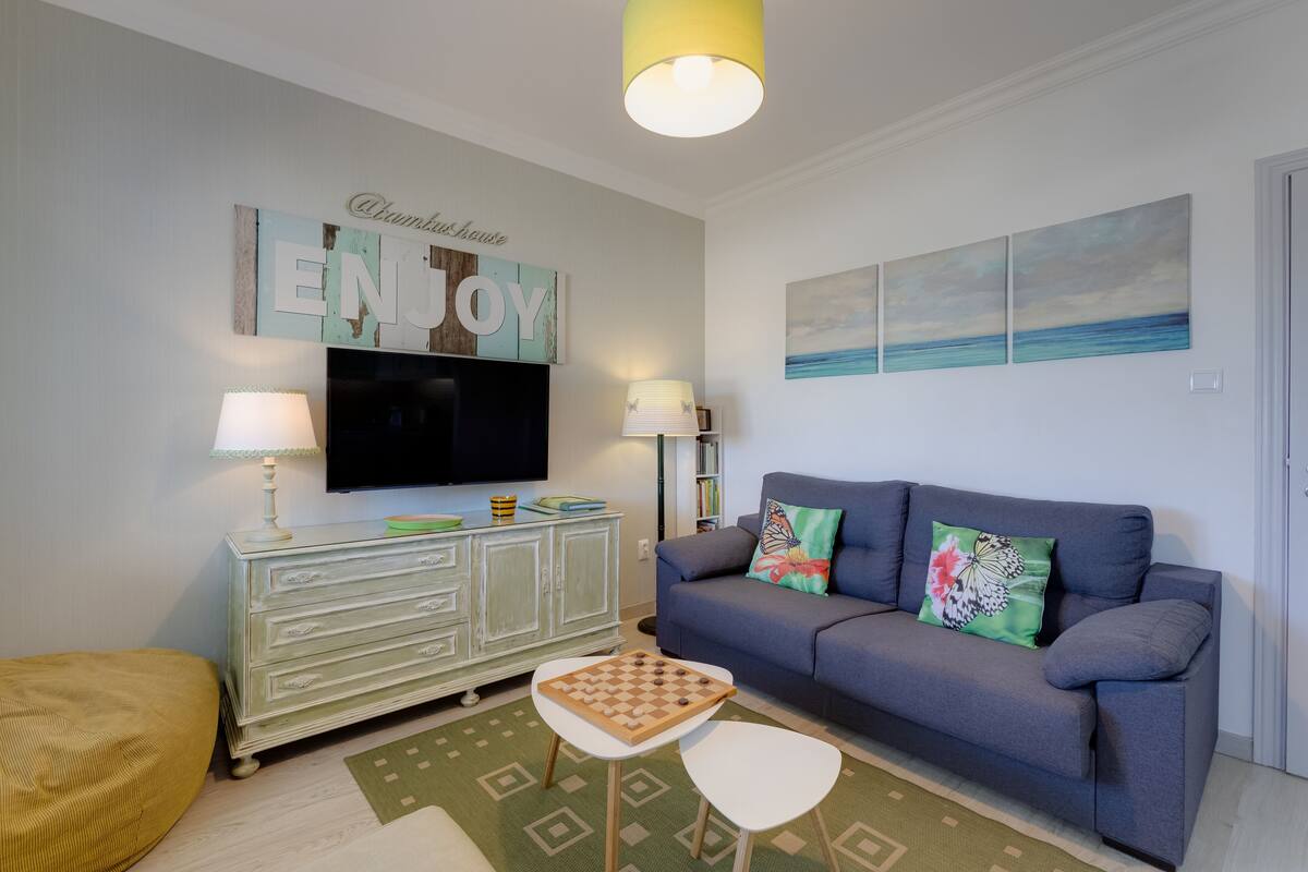 A living room with a grey sofa, a television, a cabinet, and a chessboard.