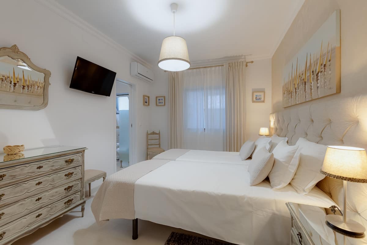 A bedroom with a large bed, bedside tables, a dresser, a TV, and a painting on the wall.