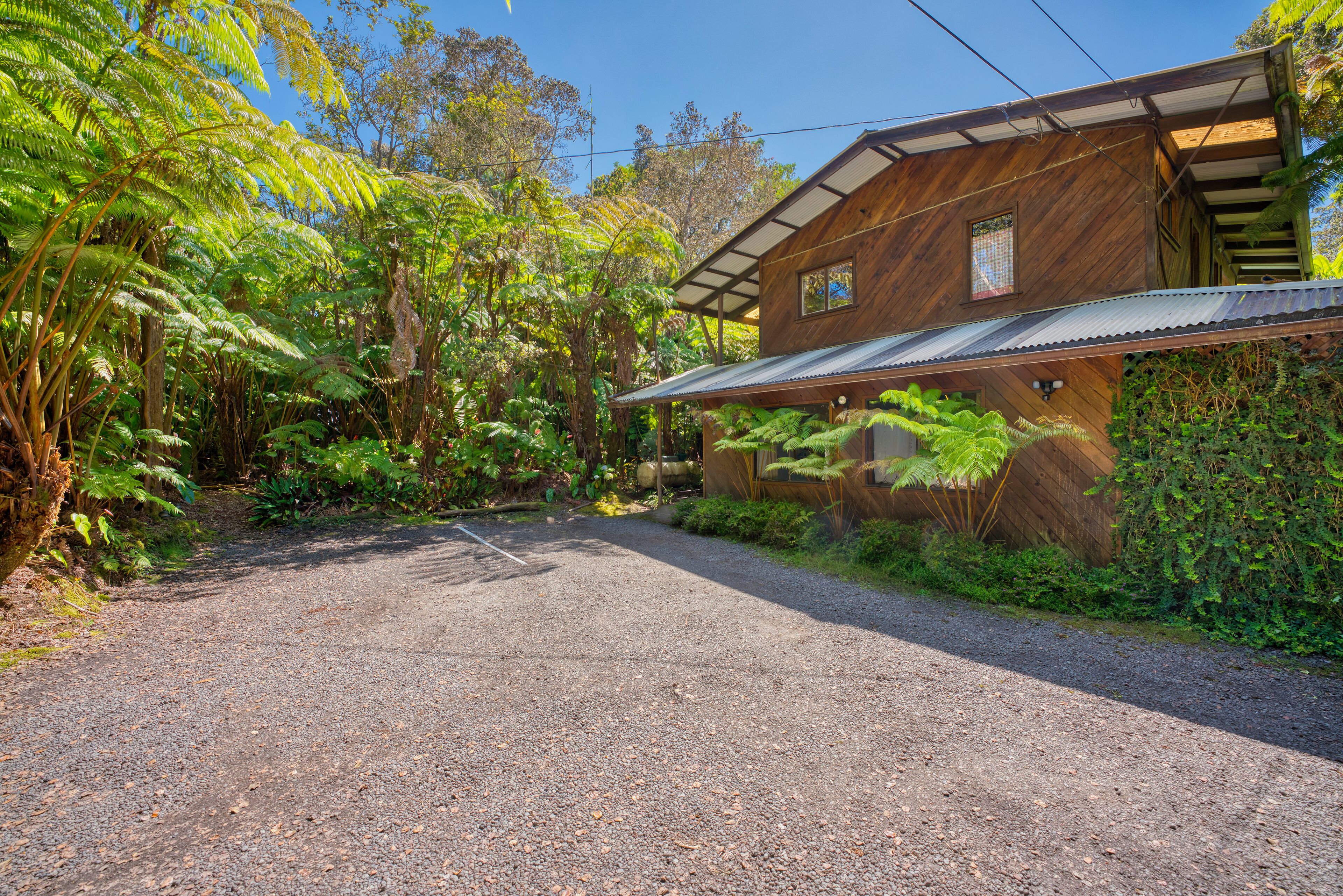 Une allée de gravier mène à une maison en bois entourée d’une végétation luxuriante.
