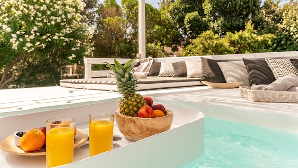 Ein Poolbereich mit Obstschale, Orangensaftgläsern und einem Korbwäschesessel.