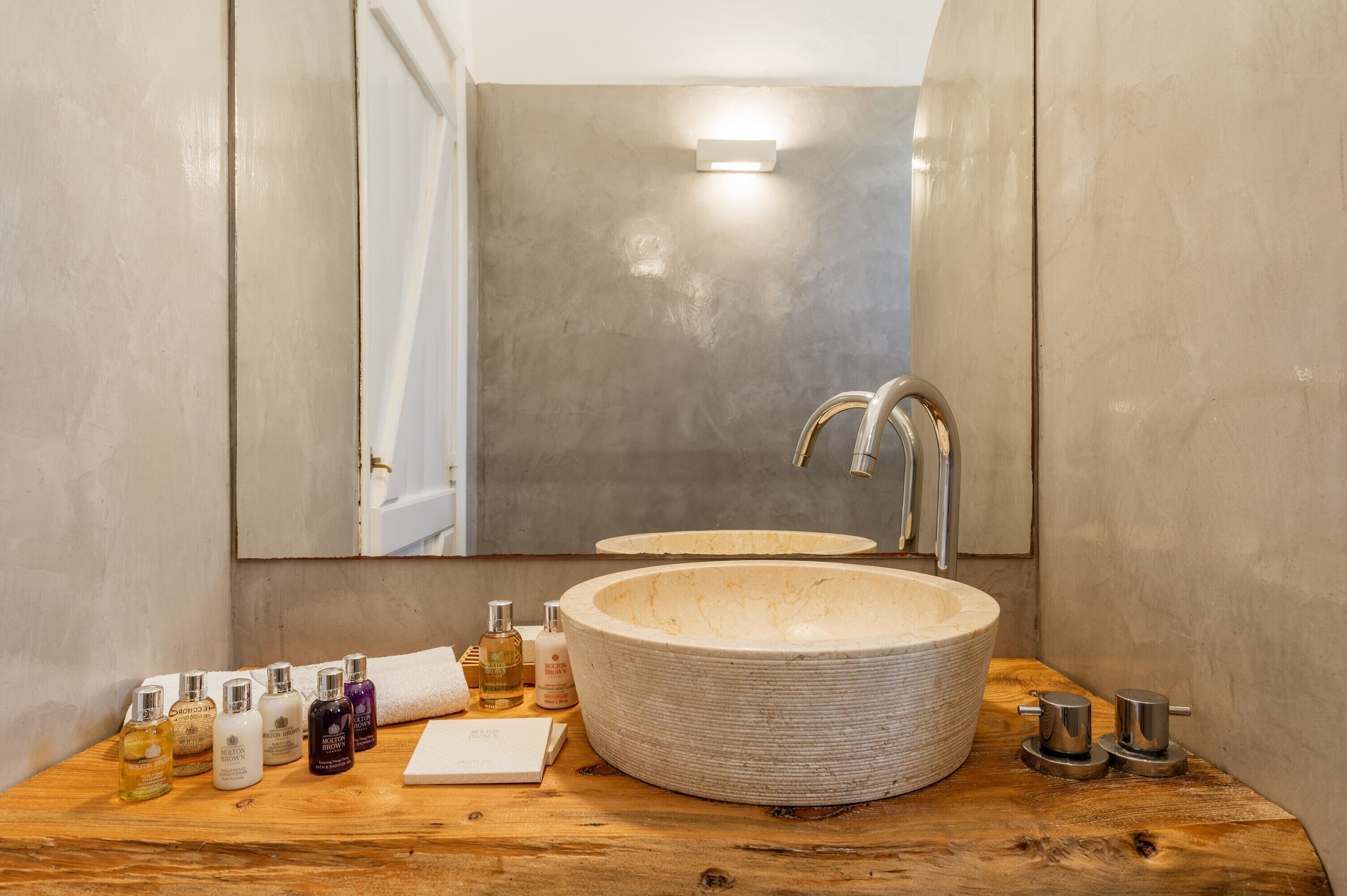A bathroom with a large, round sink, a mirror, and various toiletries on a wooden countertop.