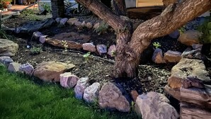 A landscaped garden with a tree surrounded by rocks and mulch, a patio area with outdoor furniture, and a building in the background. - Large house centrally located (Colorado Springs)