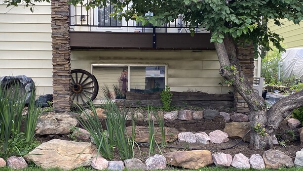 A garden with a stone border, a large wheel, and a house with a balcony. - Large house centrally located (Colorado Springs)