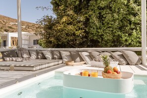Ein Poolbereich mit Liegestuhl, einem kleinen Tisch mit Obst und Saft und Blick auf eine Hügelkette.