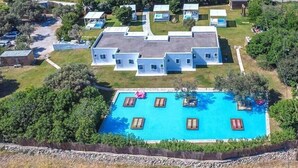 Ein großes Gebäude mit Schwimmbad, umgeben von viel Grün und Blick aufs Meer.