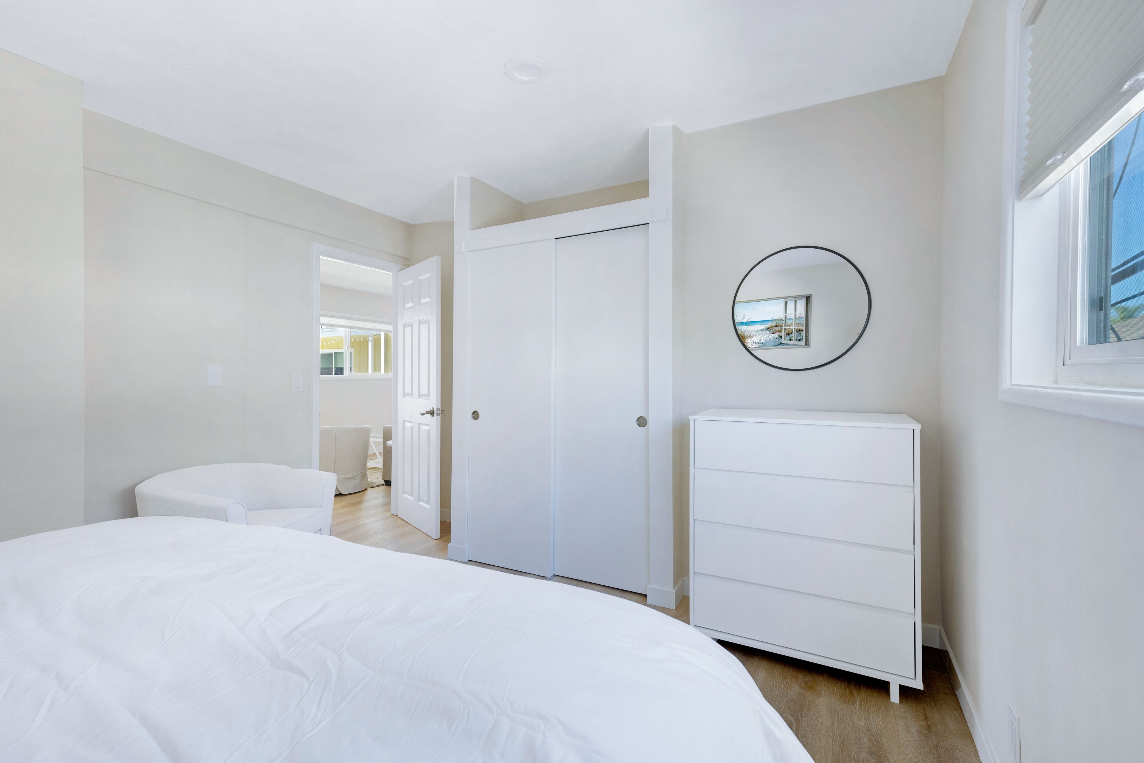 Une chambre à coucher avec un lit, une commode blanche, une armoire et un miroir au mur.