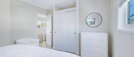 Une chambre à coucher avec un lit, une commode blanche, une armoire et un miroir au mur.