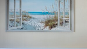 Una habitación con vista al mar a través de una ventana, un sofá blanco y una almohada con la inscripción 'Bienvenido a nuestro hogar'.