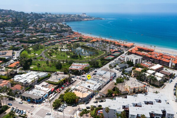 Vista aérea de un pueblo costero con playa, zonas residenciales y un parque central.