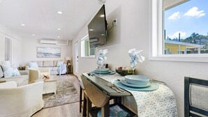 Un área de comedor con una mesa dispuesta para cuatro personas, un sofá y un televisor montado en la pared.