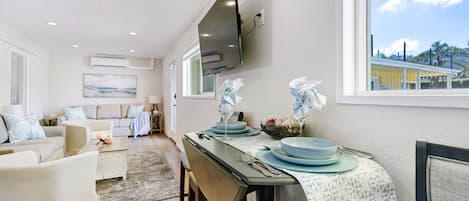 A dining area with a table set for four, a sofa set, and a TV mounted on the wall.