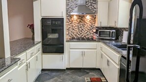Een kleine keuken met witte kastjes, een ingebouwde oven, een magnetron en een roestvrijstalen koelkast.