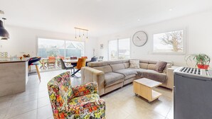 A modern living room with a sofa, colorful armchair, dining area, kitchen, and large windows. - Amazing home in Landévant with WiFi (Landévant)