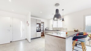 A modern kitchen with white cabinetry, a large island, and a bar area with colorful stools. - Amazing home in Landévant with WiFi (Landévant)