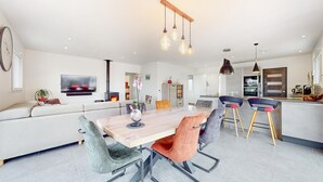 A modern living room with a large sofa, a dining table with chairs, a TV mounted on the wall, and a kitchen area with a stove and cabinets. - Amazing home in Landévant with WiFi (Landévant)