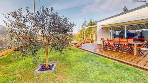 A modern outdoor patio with a wooden deck, a dining table with chairs, and a large tree. - Amazing home in Landévant with WiFi (Landévant)