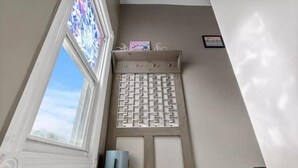 Una habitación con ventana, un biombo decorativo y una estantería de pared con un cuadro.