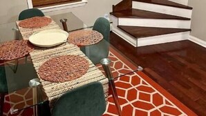 Comedor con una mesa de vidrio, sillas verdes y un tapete rojo estampado.