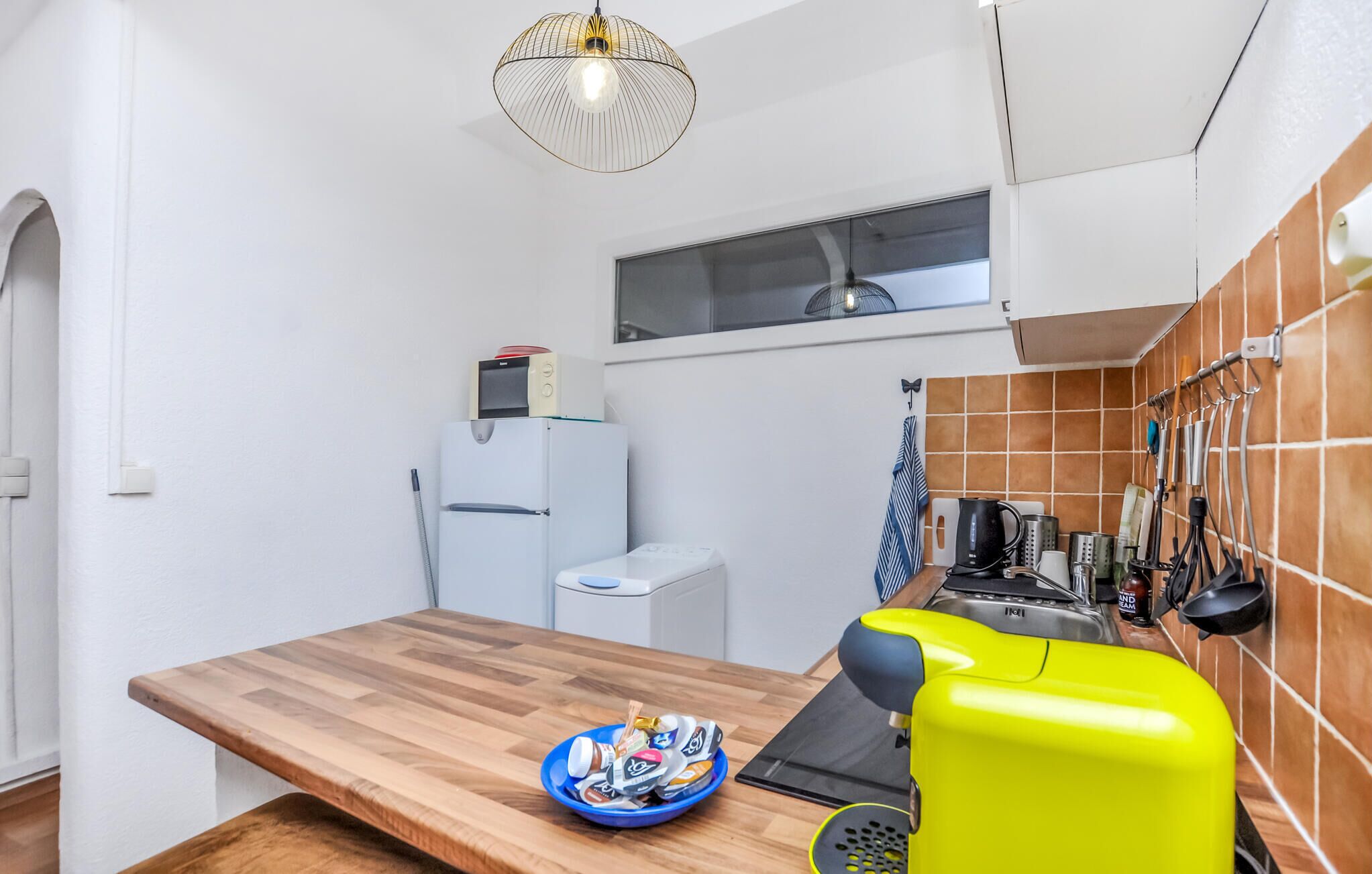 A compact kitchen with a wooden countertop, a bright yellow coffee machine, and a bowl of snacks.