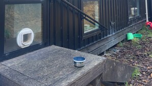 A black metal building with large windows and a wooden deck. - Maelstrom End - Eco Farm Stay Cabin (Pūponga)