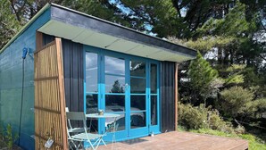 A small, modern cabin with a blue exterior, a deck, and a table with chairs outside. - Maelstrom End - Eco Farm Stay Cabin (Pūponga)
