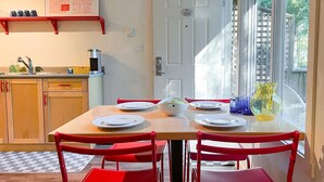 A kitchen with a dining table set for four, red chairs, and a window with a view of greenery. - The Stonewater (Madeira Park)