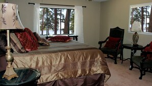 Een slaapkamer met een groot bed, twee stoelen, een tafeltje en een raam met uitzicht op bomen.