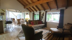 Een gezellige woonkamer met een houten plafond, een bank, een eettafel met stoelen en een open haard.
