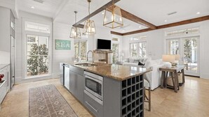 A spacious kitchen with a large island, built-in oven, and a wine rack. There is a dining area with a table and chairs, and a living room with a sofa and a TV. - STEPS to Camp WaterColor! 6-Seater LSV/Golf Cart, 4 Bikes Included! (Santa Rosa Beach)