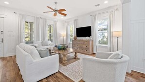 A spacious living room with a ceiling fan, white furniture, a wooden coffee table, and a flat-screen TV. - WaterColor NEXT to Pool w NEW 6-Seater LSV 4 Bikes, Amenity Access Included! Pet Friendly! (Santa Rosa Beach)