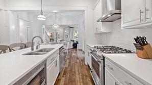 A modern kitchen with white cabinetry, a central island with a sink, a stove, and a knife block. - WaterColor NEXT to Pool w NEW 6-Seater LSV 4 Bikes, Amenity Access Included! Pet Friendly! (Santa Rosa Beach)