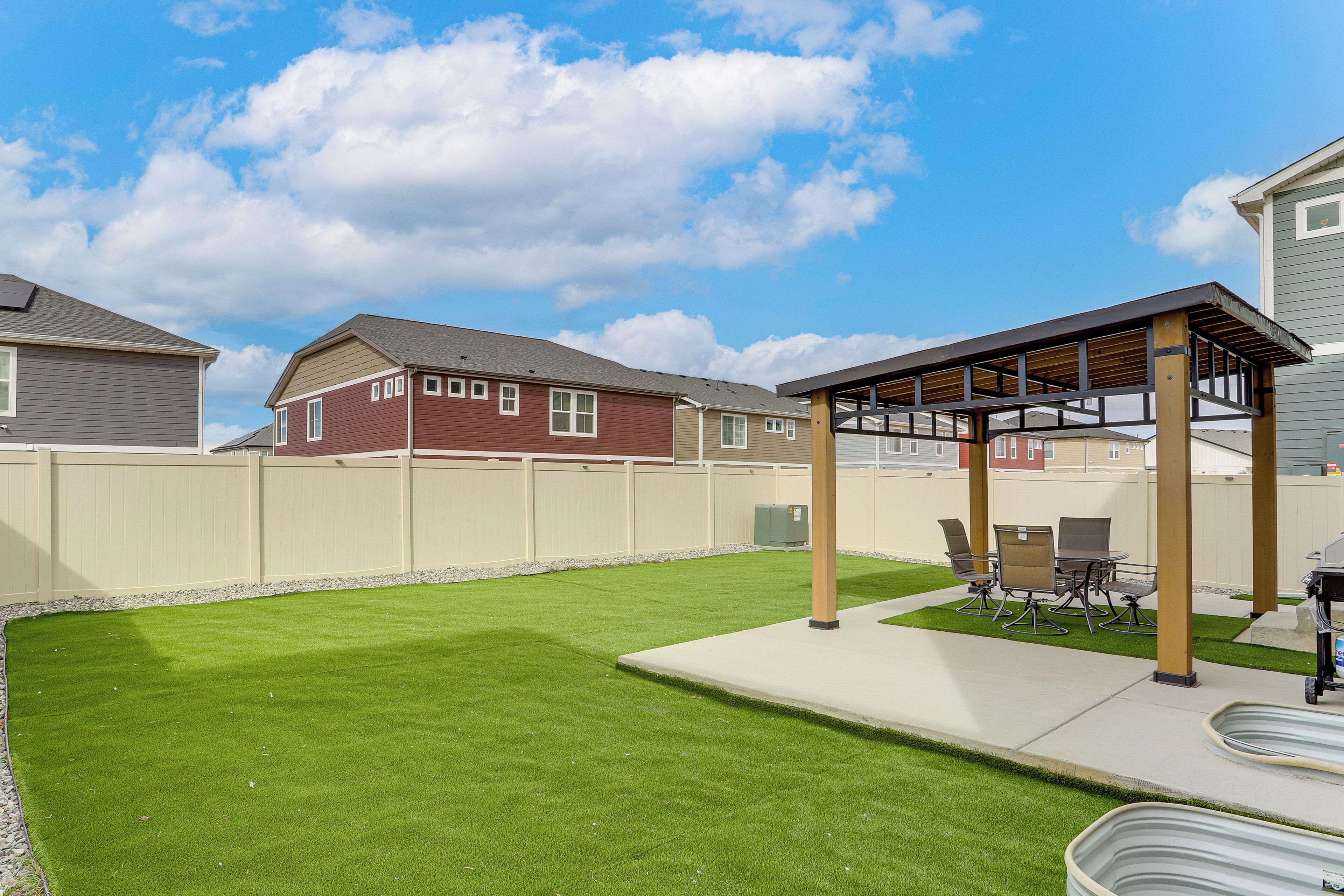 A backyard with artificial grass, a pergola, outdoor furniture, and a barbecue area.