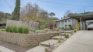 A residential property with a stone retaining wall, a wooden fence, and a well-maintained garden with various plants and a small patio area. - Pacheco/Martinez Studio: 22 Mi to Dtwn Oakland! (Pacheco)