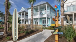 A beachfront property with a surfboard, a wooden signpost with directional signs, and a two-story building with balconies.