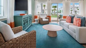 Un salon moderne doté d’un téléviseur à écran plat, de meubles en osier, d’une table basse ronde et offrant une vue sur une piscine et des palmiers.