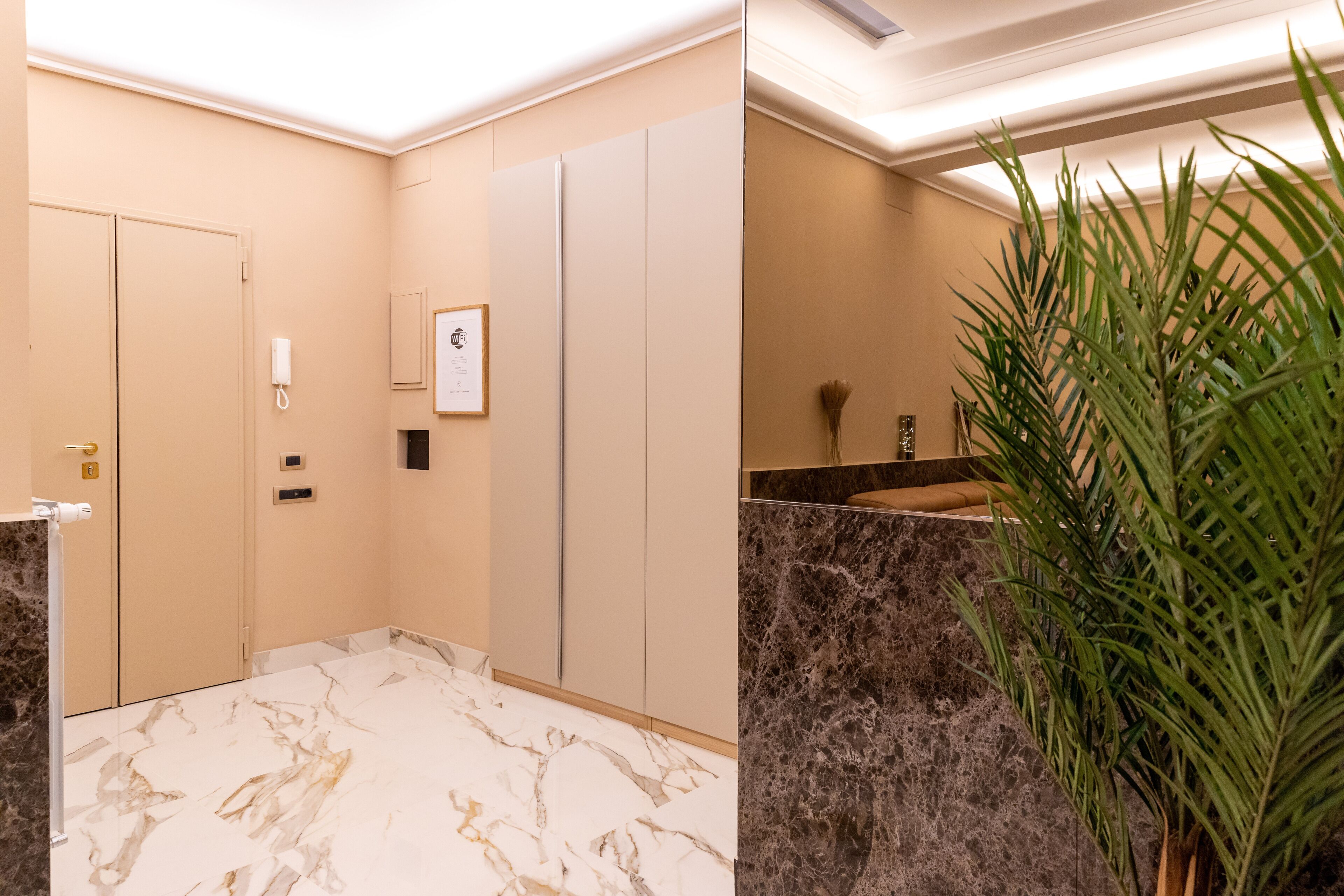 A hotel bathroom with marble flooring, a sink, a mirror, and a plant.