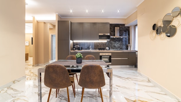 Een moderne keuken met een marmeren vloer, een eettafel met stoelen en een keukeneiland met een spoelbak en kookplaat.
