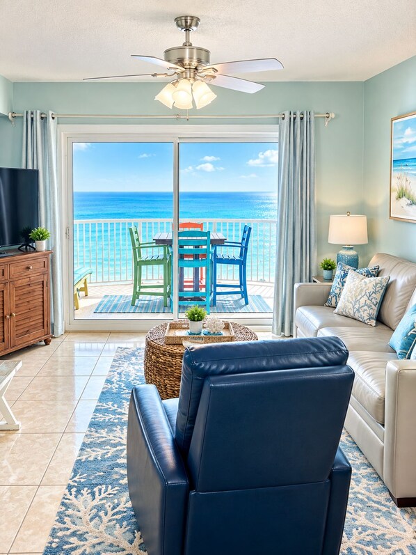A living room with a view of the ocean, a ceiling fan, a television, and a sofa.