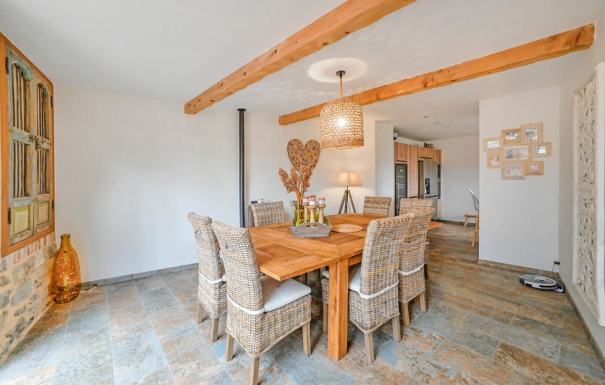 A dining area with a wooden table and wicker chairs, a hanging light fixture, and a tiled floor.