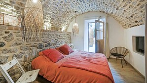 Een slaapkamer met een stenen muur, een bed met rode beddengoed, een hangende lamp en een televisie aan de muur.