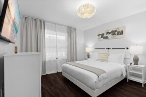 A modern hotel room with a large bed, bedside tables, a flat-screen TV, and a painting on the wall.