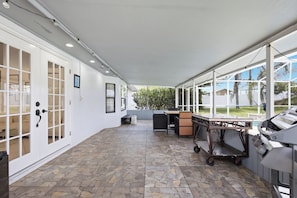 A covered patio area with stone flooring, a grill station, and a seating area with a table and chairs. - Sunshine Villa:3BR Home with Sparkling Heated Pool/Huge Backyard (Davenport)