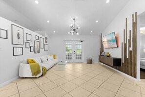 A modern living room with a white sofa, a glass coffee table, and a flat-screen TV mounted on a wooden wall.