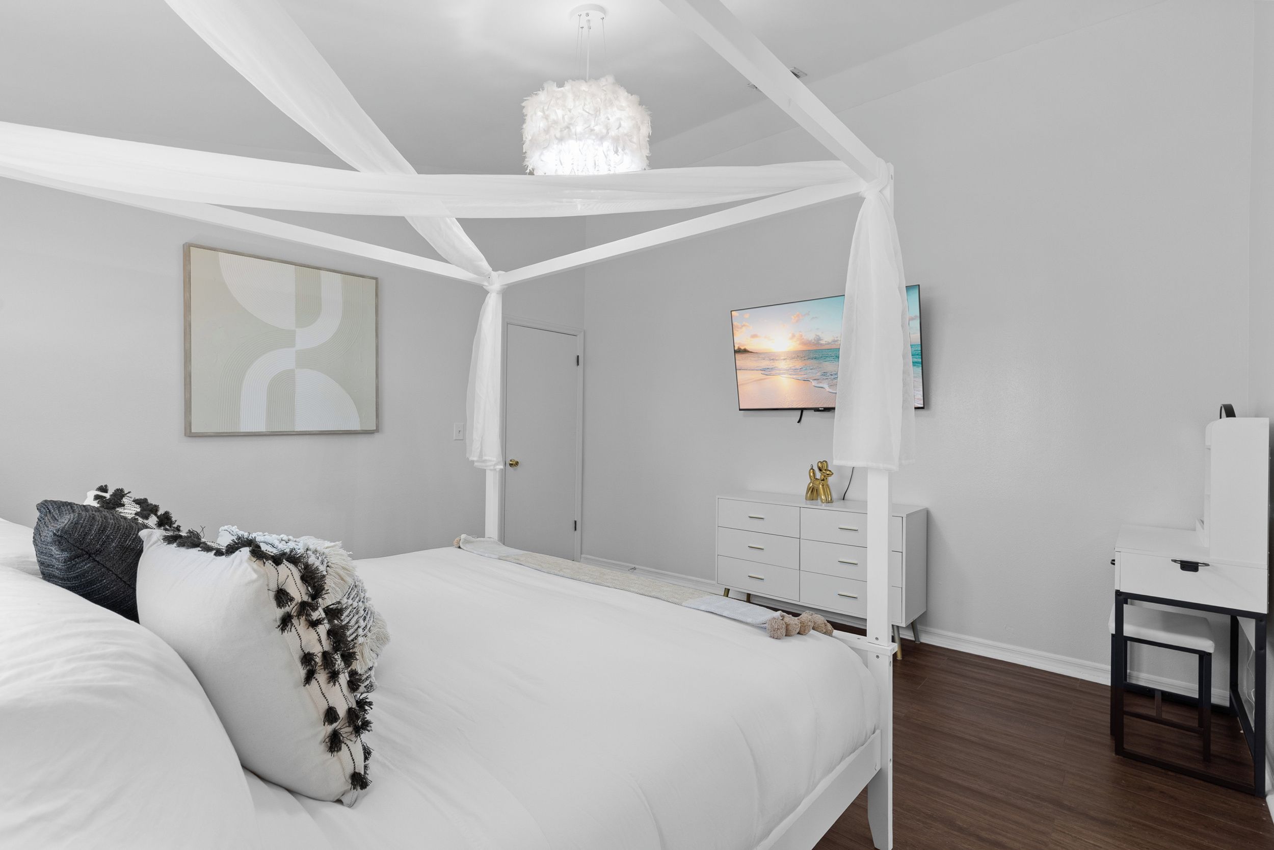 Ein Schlafzimmer mit Baldachinbett, Flachbildfernseher, Kommode und Schreibtisch mit Stuhl.