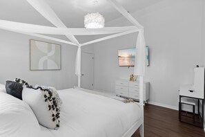 A bedroom with a canopy bed, a flat-screen TV, a dresser, and a desk with a chair. - Sunshine Villa:3BR Home with Sparkling Heated Pool/Huge Backyard (Davenport)