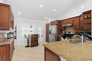 A modern kitchen with granite countertops, stainless steel appliances, and wooden cabinetry. - Sunshine Villa:3BR Home with Sparkling Heated Pool/Huge Backyard (Davenport)
